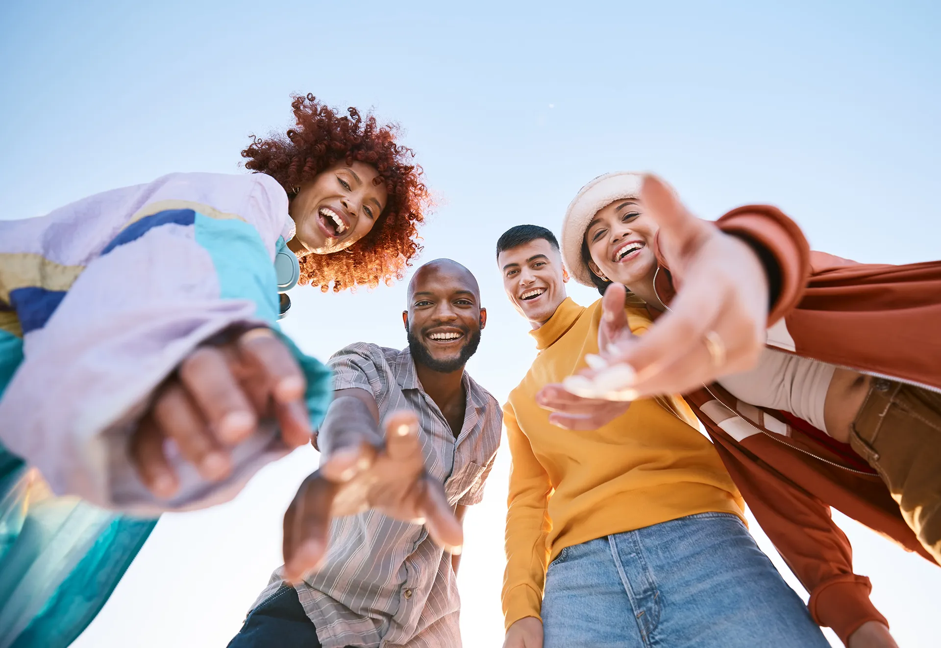 Group of diverse friends looking down at the camera, smiling and reaching out, suggesting unity and friendship