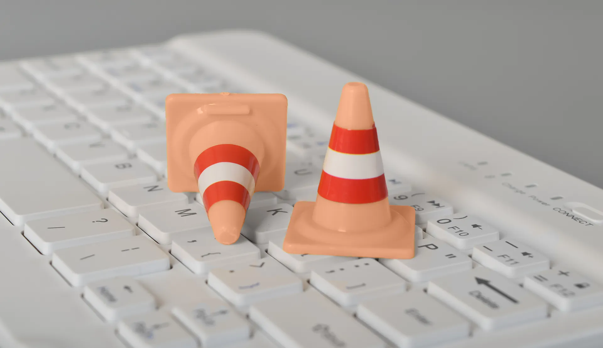 Two miniature traffic cones placed on a white keyboard, symbolizing a potential caution or warning in a digital context.